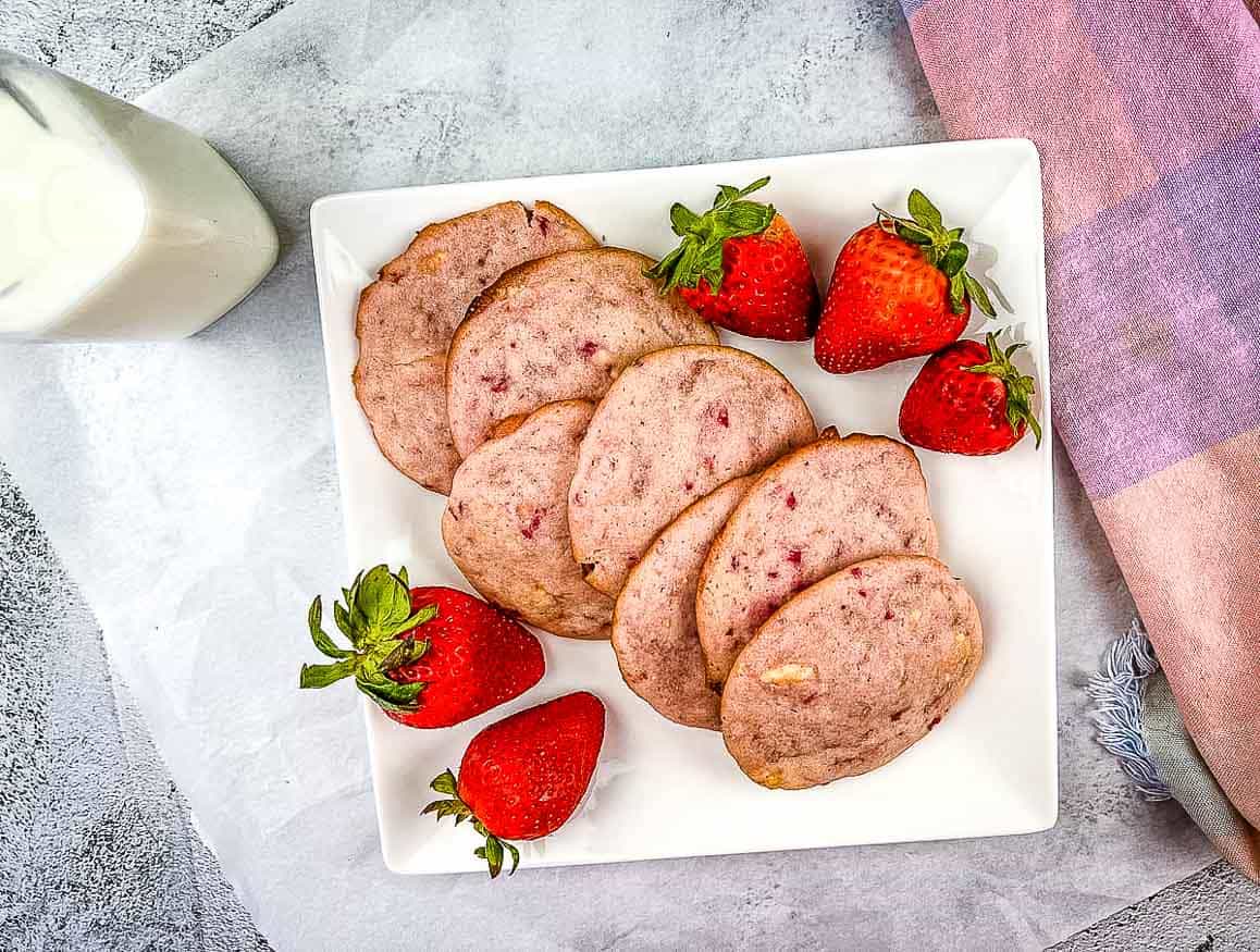Strawberry Shortcake Cookies on a white plate with strawberries nearby.