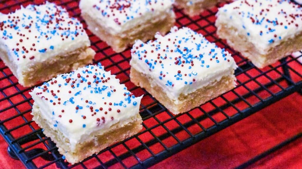 Red, white and blue sugar cookie bars cut into squares on a baking rack.