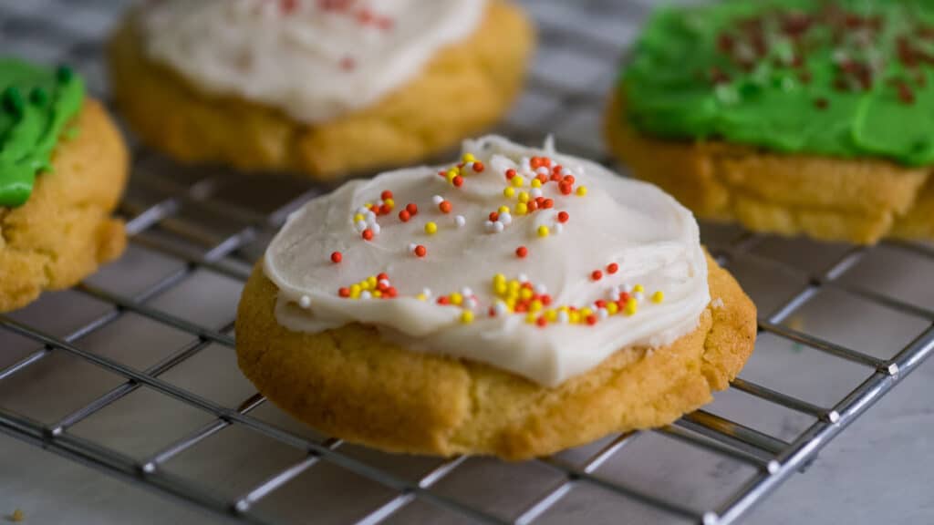 Sugar cookies with white or green frosting and sprinkles on a baking rack.