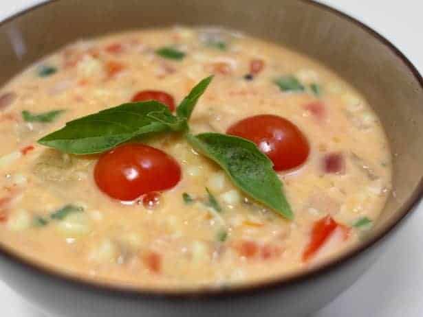 a bowl of corn and tomato soup with fresh basil.