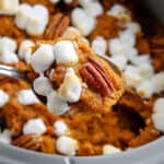 Crock pot with sweet potato casserole with pecans and marshmallows.