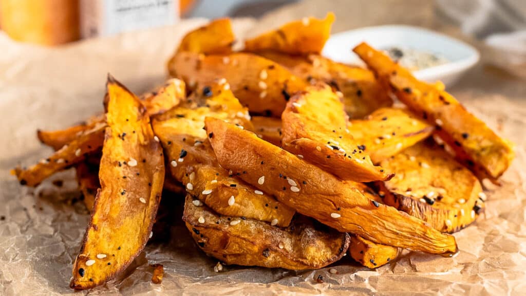 Sweet potato wedges coated in everything bagel seasoning on brown paper.