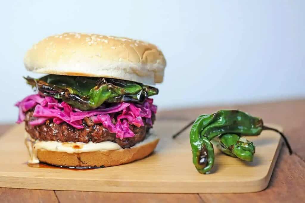 Burger topped with grilled shishito peppers and purple cabbage.