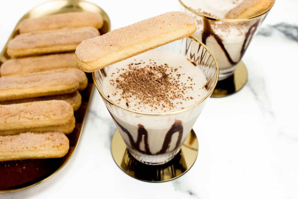 a tiramisu martini with chocolate sauce and a ladyfinger garnish on a gold coaster.