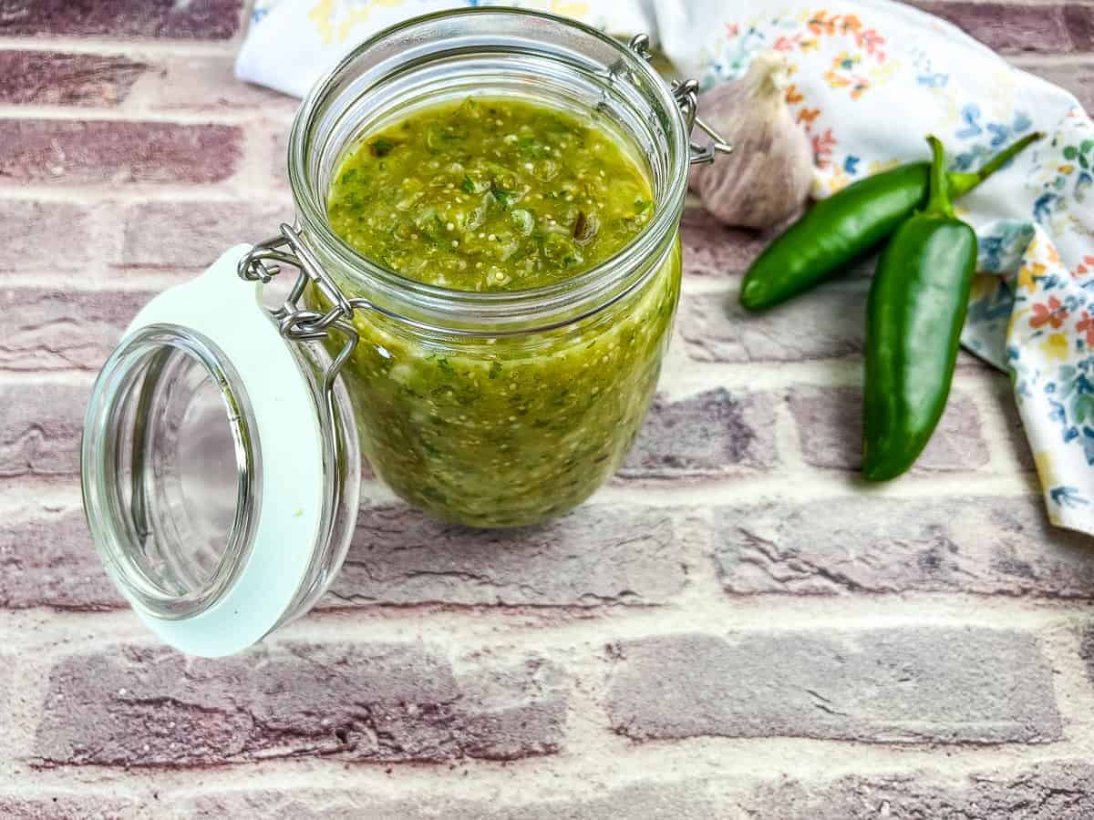 An image of Roasted Tomatillo Sauce in a jar with jalapenos nearby.