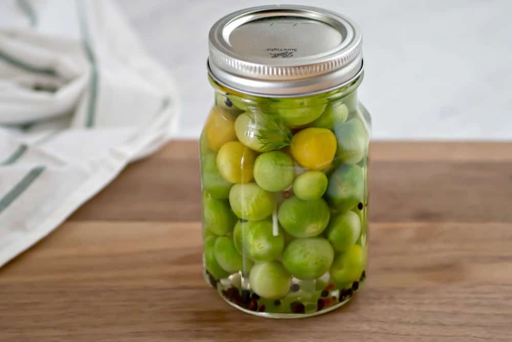Jar of pickled green cherry tomatoes on a wooden cutting board.