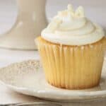 Vanilla cupcake with frosting on white china plate.