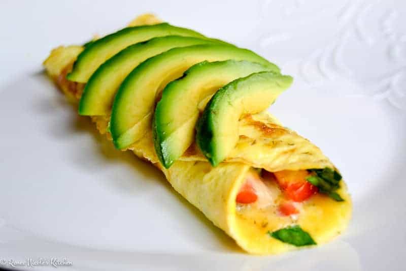 A veggie omelet on a white plate topped with fresh avocado.