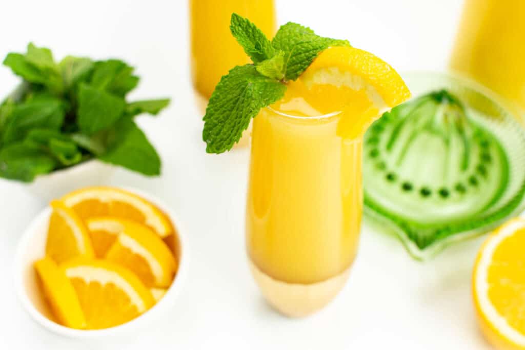 an orange juice mimosa on a mimosa bar with mint and orange wedges.
