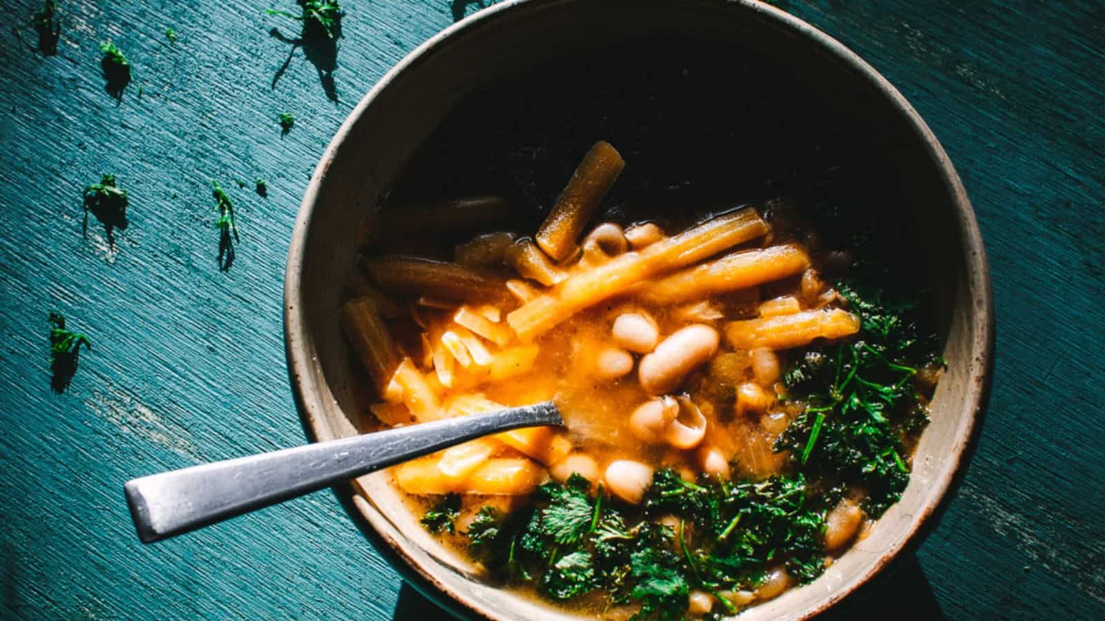 Top view of a ceramic bowl filled with white beans, cheese and green herbs.