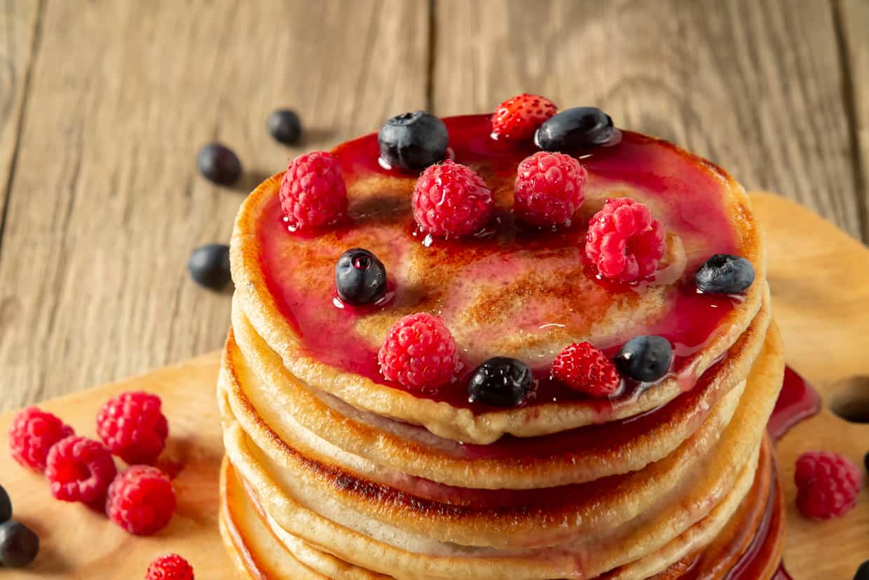 A stack of pancakes topped with raspberry syrup and fresh berries.