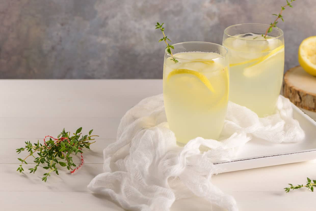 two glasses of lemonade garnished with thyme sprigs, resting on white plates.