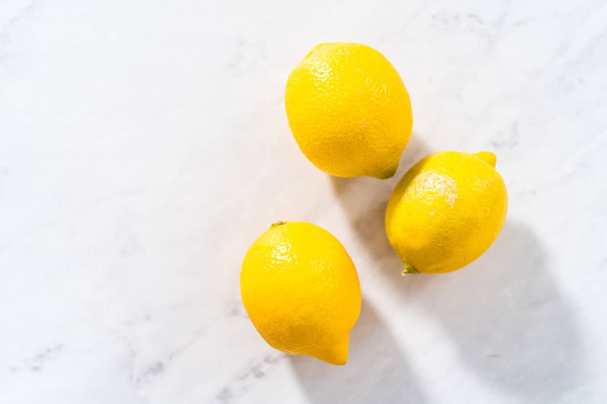 three lemons casting shadows on a marble countertop.
