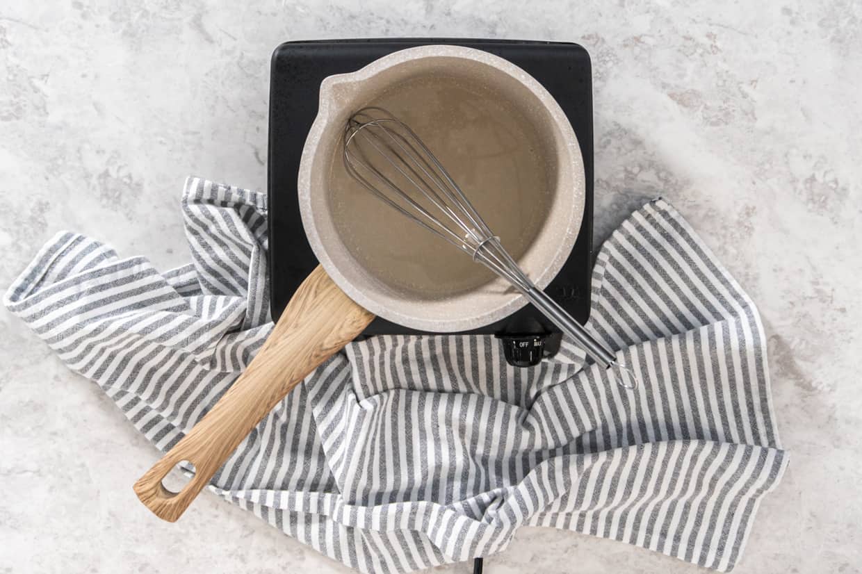 A whisk in a saucepan of simple syrup on a portable burner.
