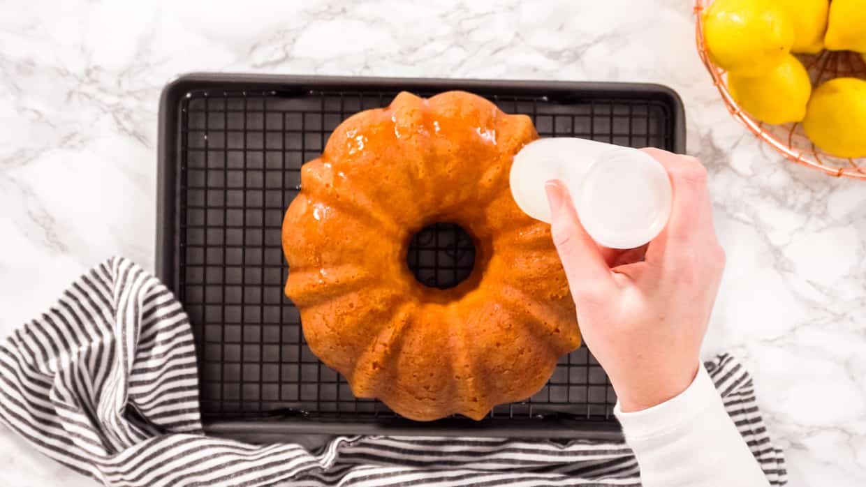 A hand squeezes simple syrup onto a bundt cake.