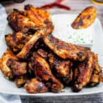 Pile of BBQ chicken wings on a white plate with dipping sauce.