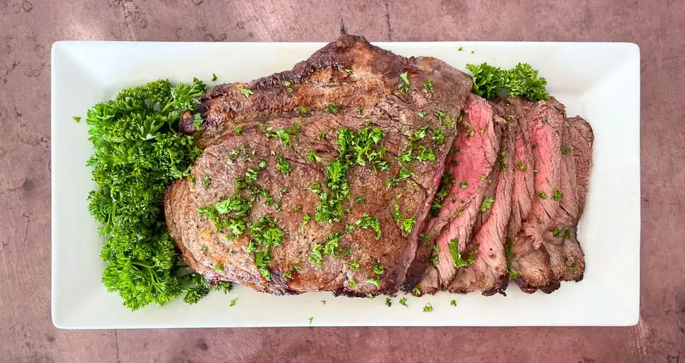 London broil on a white platter with parsley.