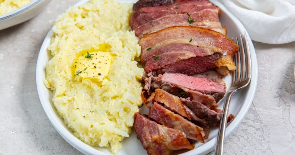 bacon wrapped ribyee on a plate with mashed cauliflower