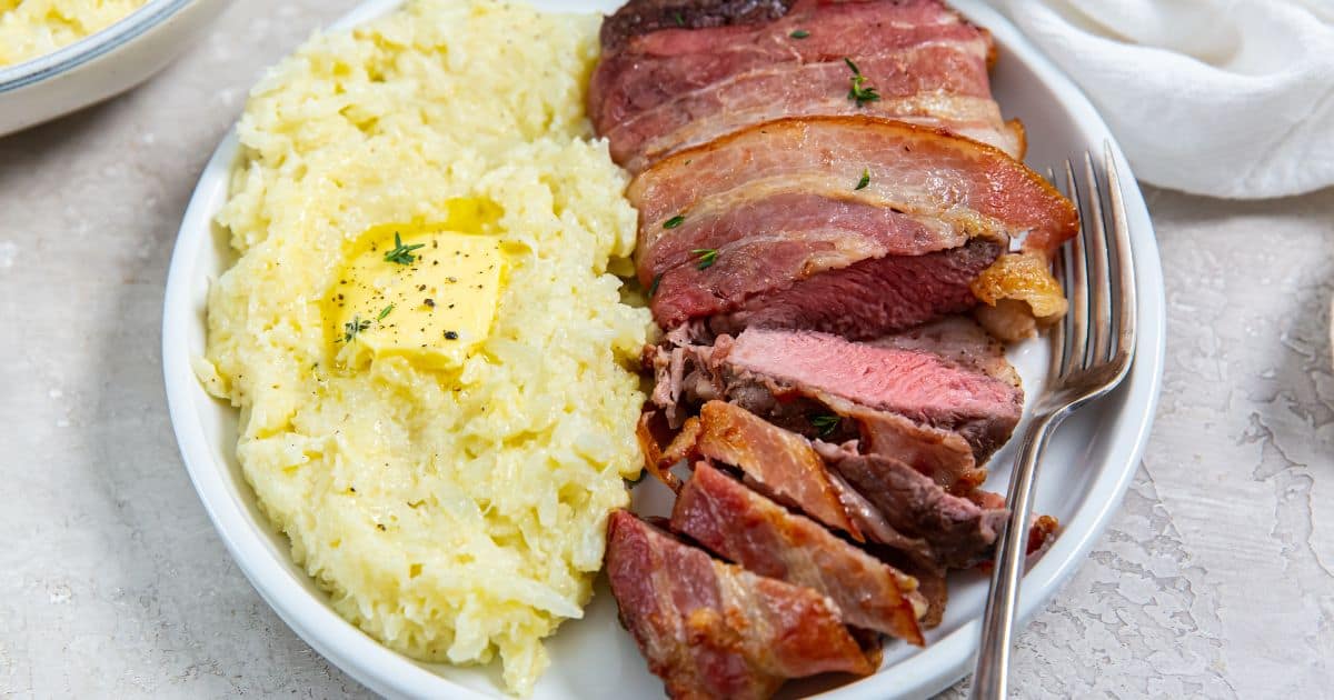 Air Fryer Bacon Wrapped Ribeye Steak with rice, butter and thyme on a white plate.