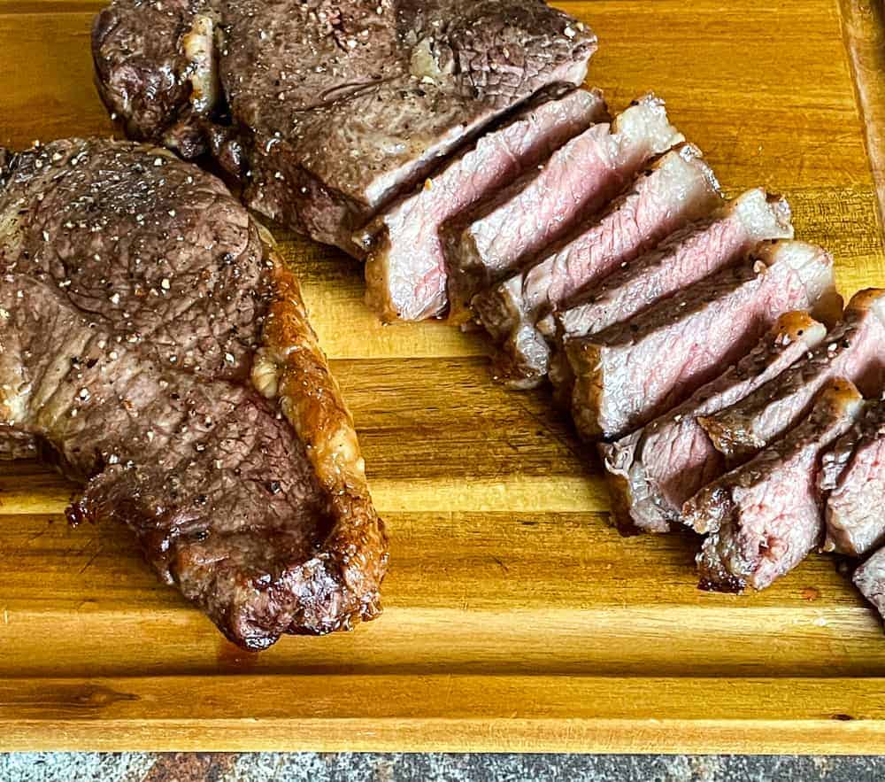 Two new york steaks on a board, one of them is sliced.