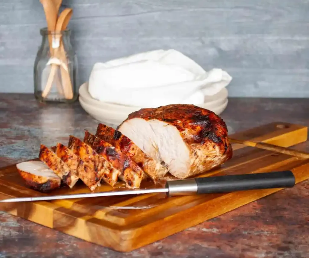 A turkey breast on a cutting board and partly sliced.