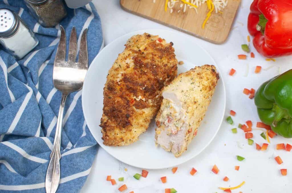 A sliced open stuffed chicken breast on a white plate with an air fyer in the background.