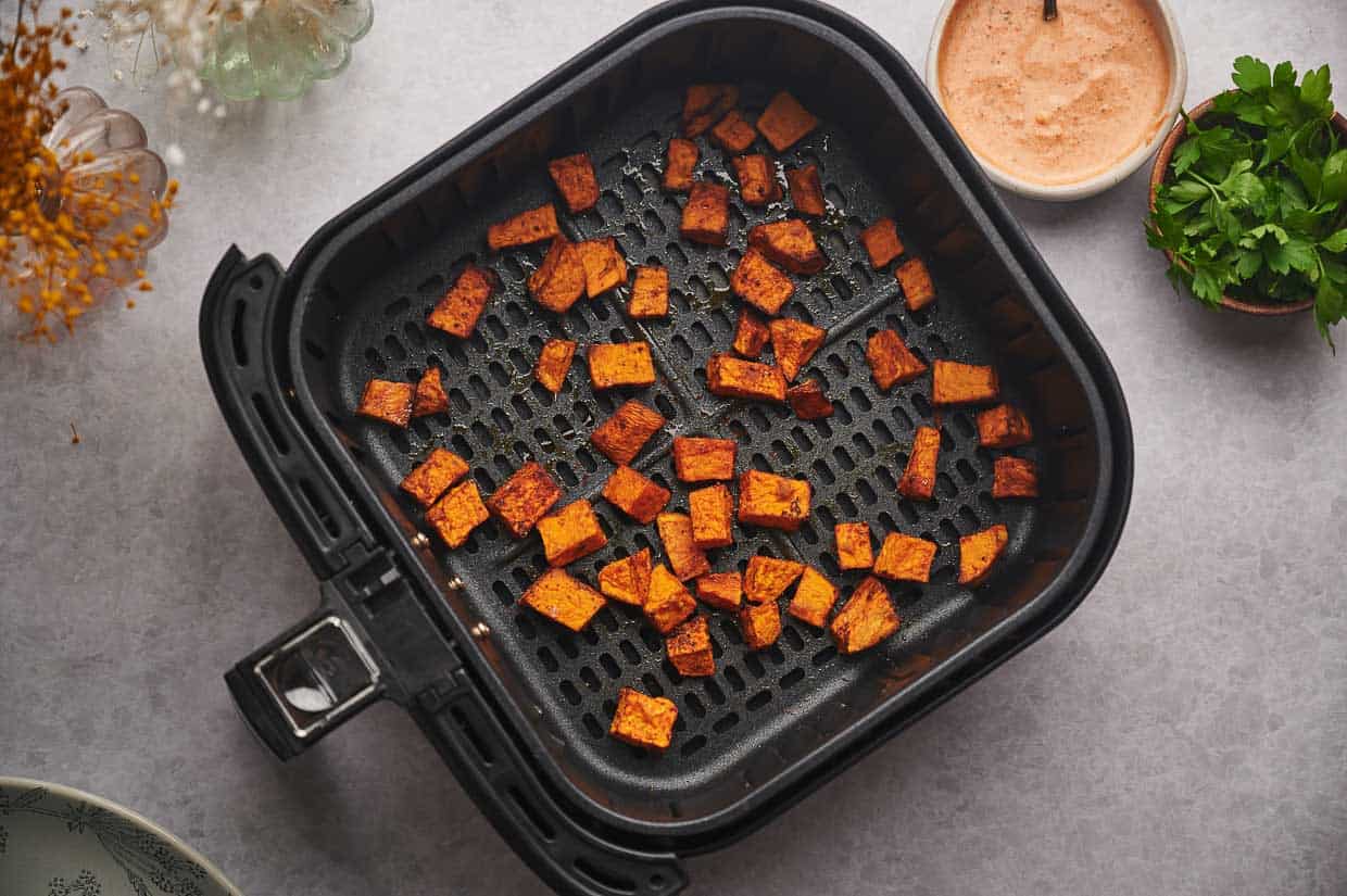 Cooked sweet potato cubes in an air fryer basket.