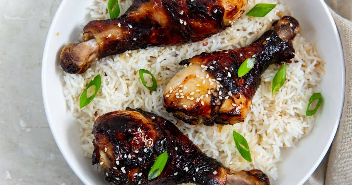 Crispy Air Fryer Teriyaki Chicken Legs in a white bowl with white rice, green onions, and sesame seeds.