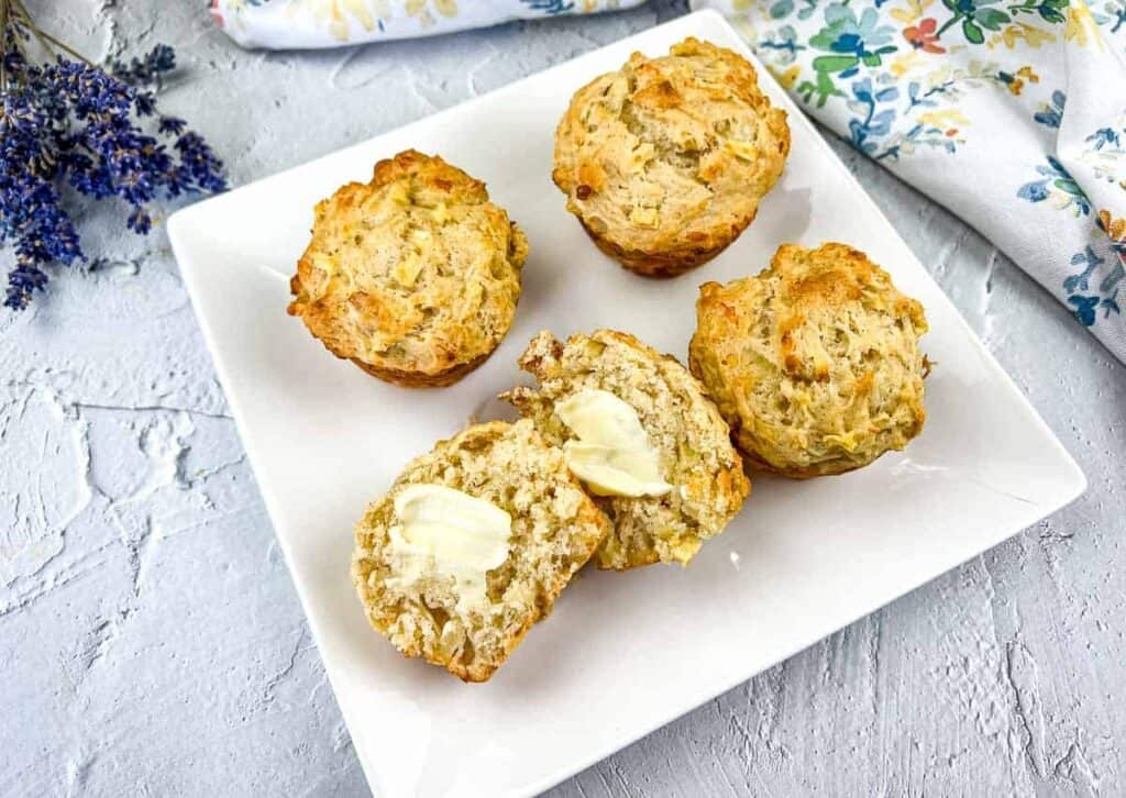 Apple Cheddar Muffins on a white square plate with a cut muffin in the front.