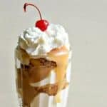 Image shows a close up of an Apple Pie Parfait in a milkshake glass topped with whipped cream and a cherry.