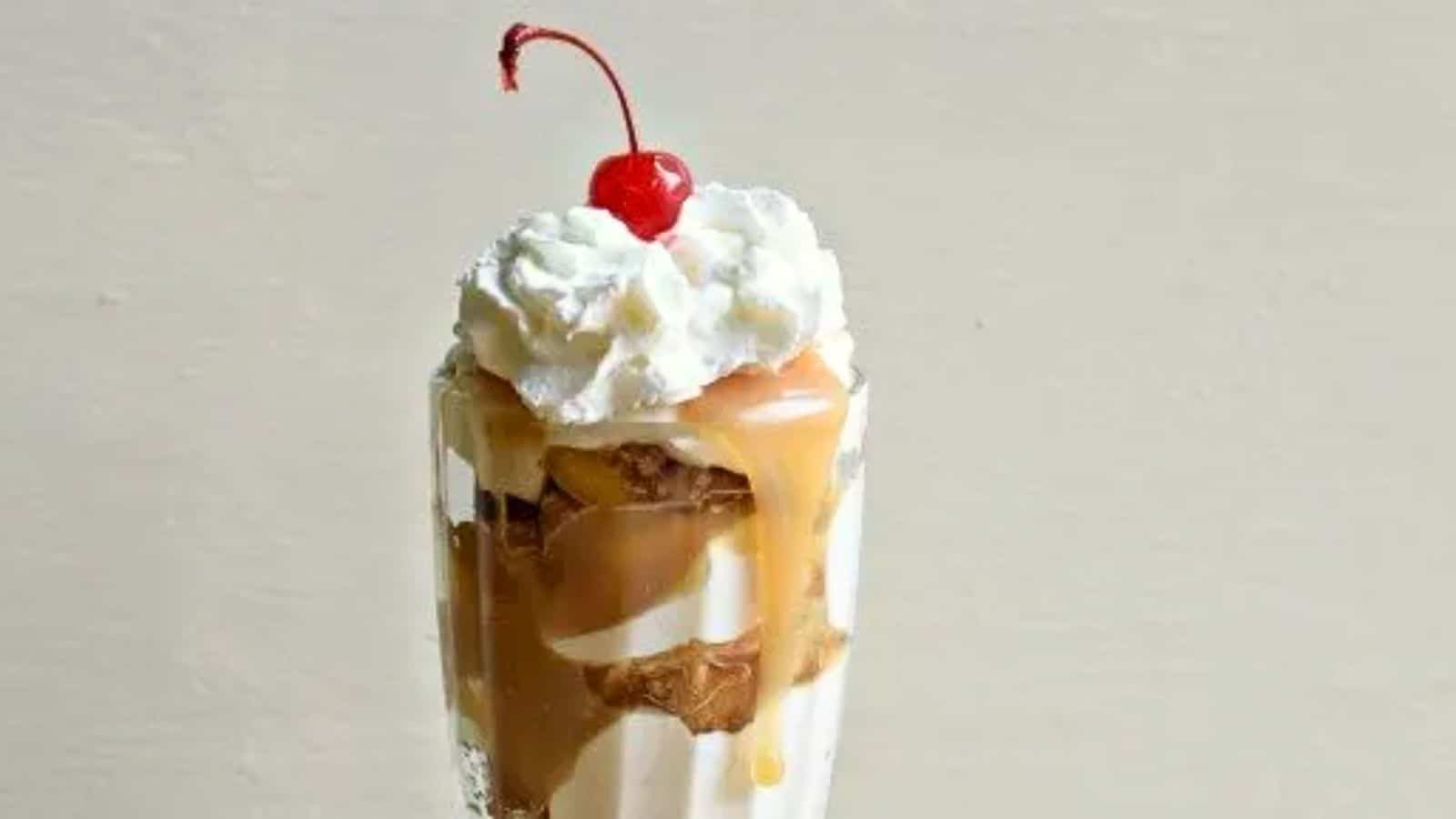 Image shows a close up of an Apple Pie Parfait in a milkshake glass topped with whipped cream and a cherry.