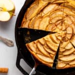 An apple cake baked in a cast iron skillet, cut into slices.