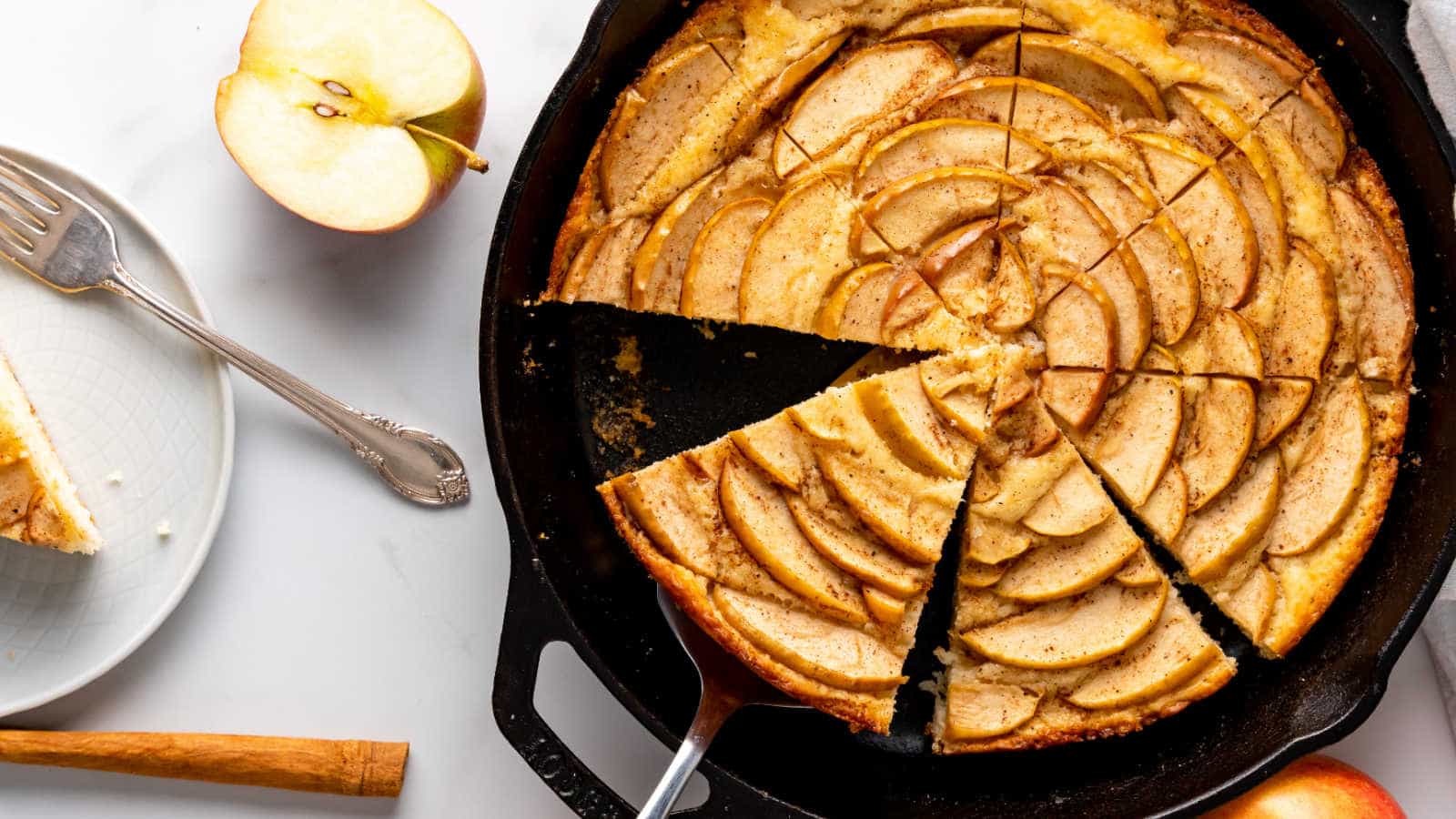 An apple cake baked in a cast iron skillet, cut into slices.