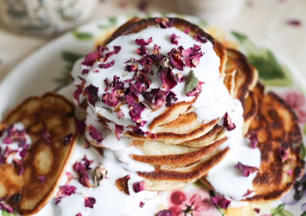 Russian pancakes with rose petals and kefir on a white plate.