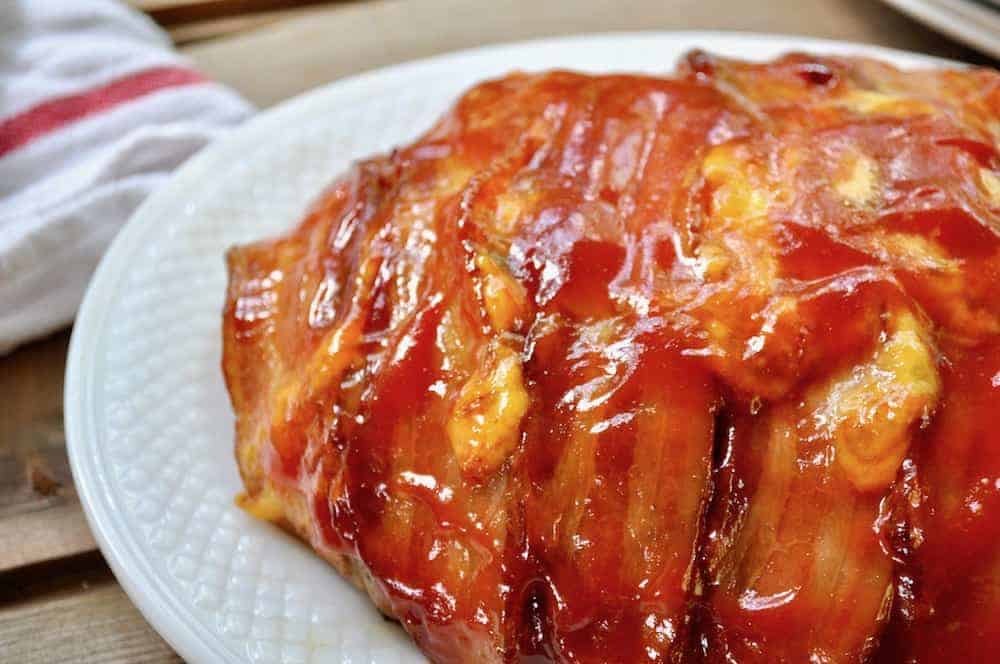 Meatloaf wrapped in bacon and glazed with ketchup on a white platter.