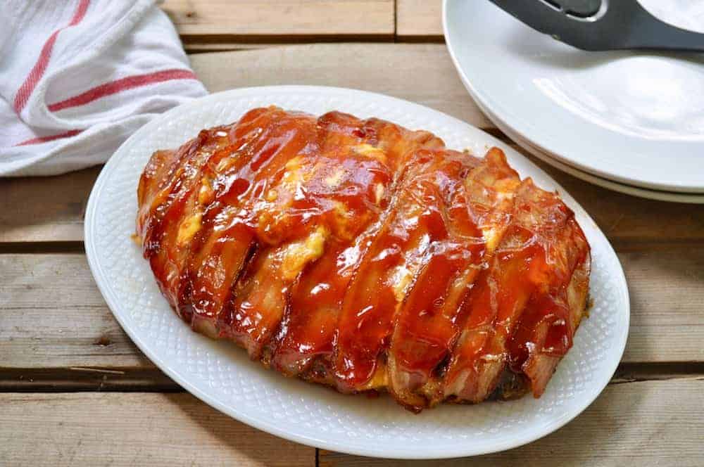 Bacon wrapped meatloaf on a white platter with a bbq glaze.