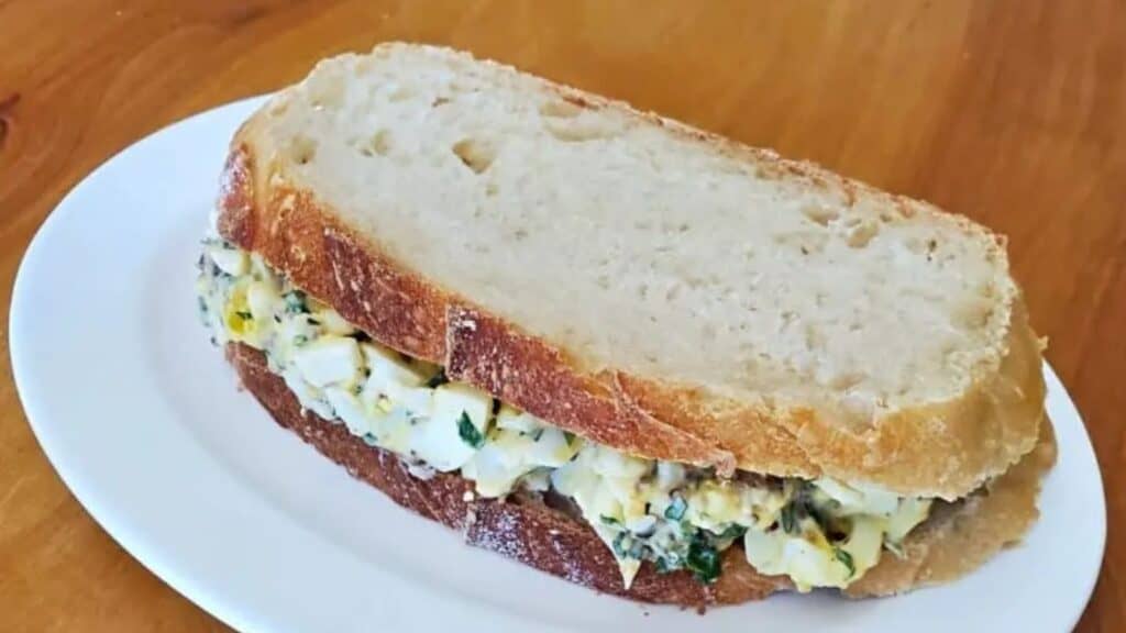 Image shows a Bacon Egg Salad sandwich on a white plate.