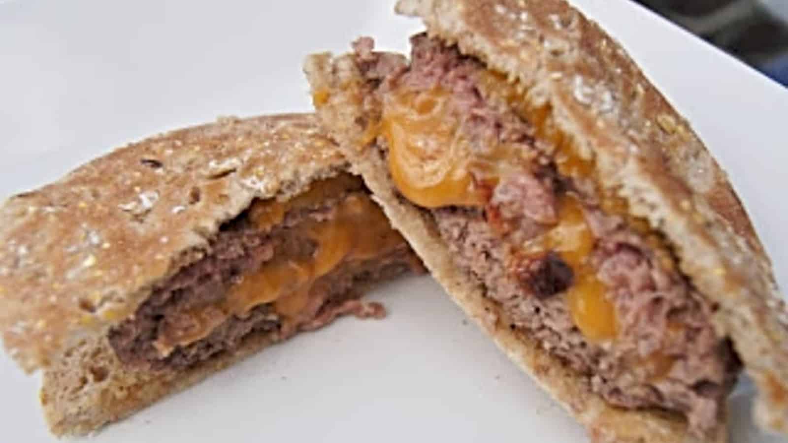 Bacon cheddar stuffed burger cut in half and on a white plate.