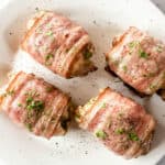 Four bacon-wrapped chicken thighs with parsley garnish on white plate.