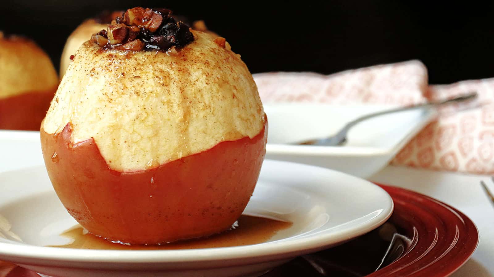 A baked apples on a white plate with a glaze dripping onto a plate.