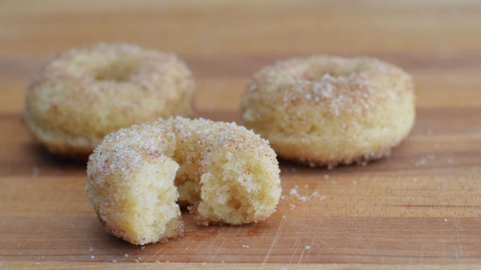 Image shows Baked cinnamon sugar donuts on a wooden table.