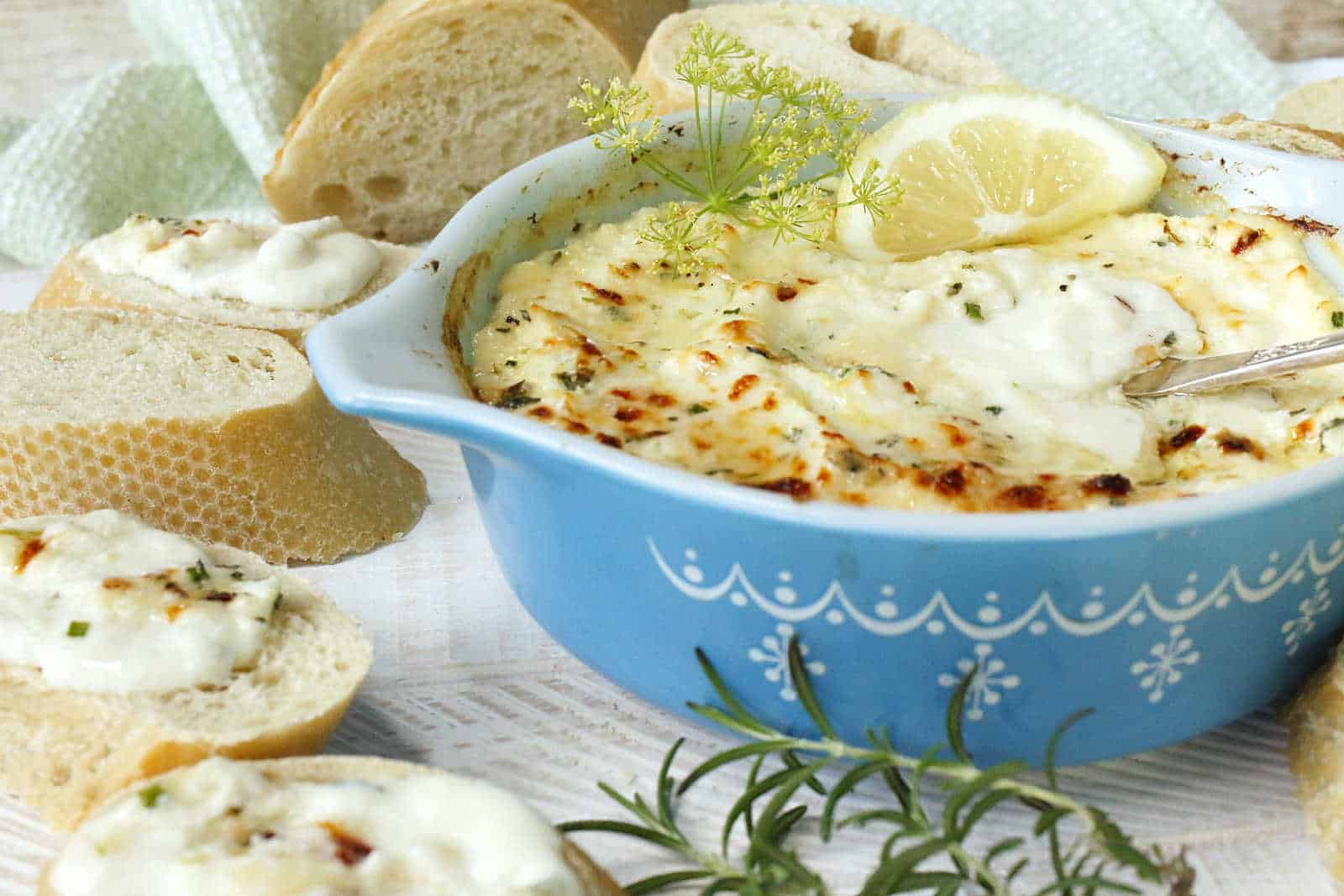 Baked ricotta cheese in a blue casserole dish with sliced bread.