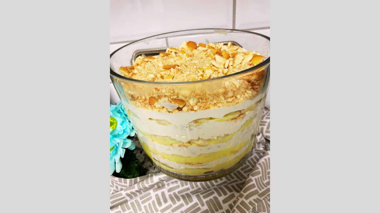 Layered banana pudding in clear trifle bowl with crushed Nilla Wafers on top.