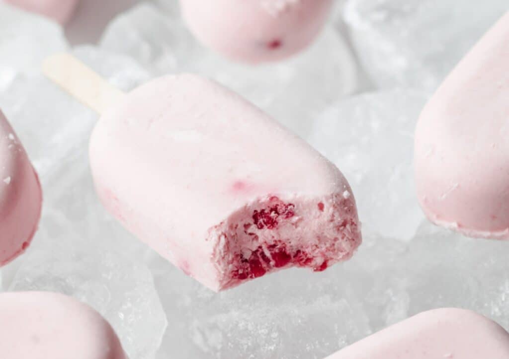 A berries and cream keto popsicle with a bite taken out of it.