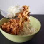 Image shows a Bite of tomato lime chicken on a fork with rice and the rest of the bowl in the background.