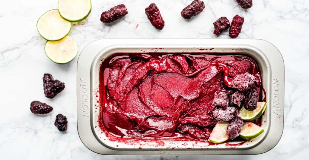 Horizontal image of blackberry lime sorbet in a metal loaf pan on a marble background.