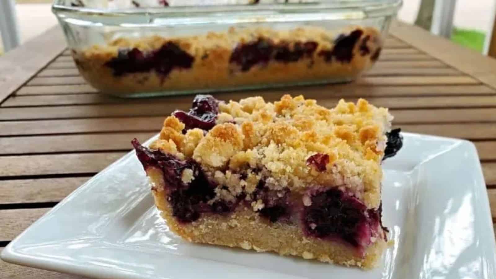 Image shows a Blueberry Crumb Bar on a plate with the full container behind it.