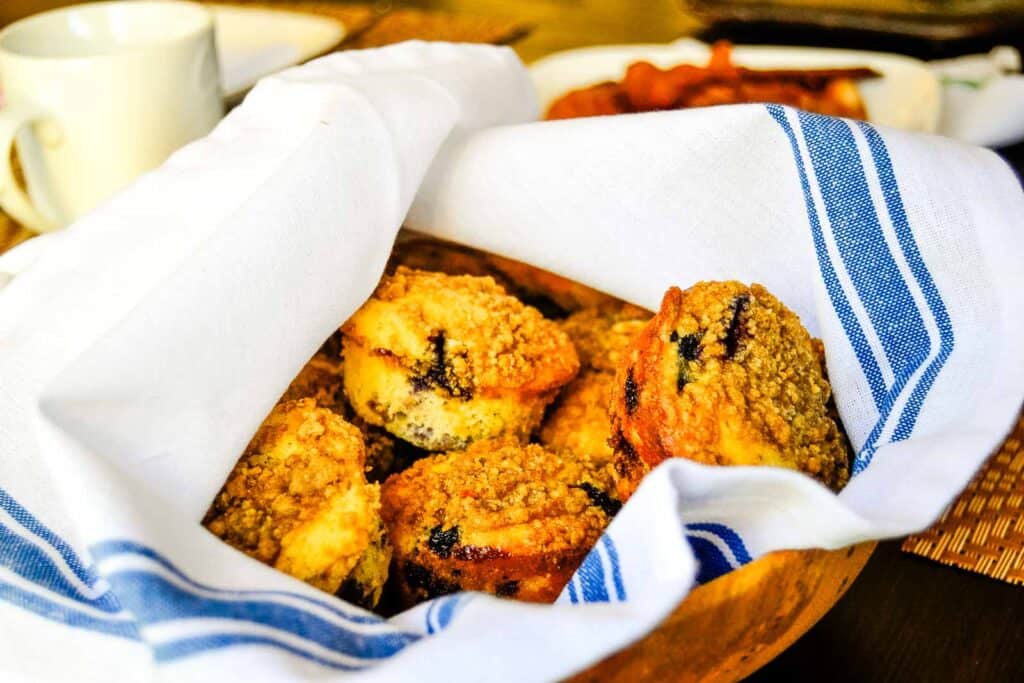 Blueberry muffins in a basket, wrapped in a white and blue towel. 