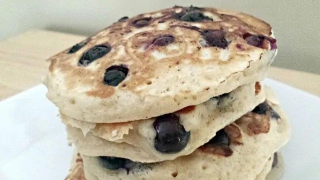 Image shows blueberry pancakes stacked on a white plate.