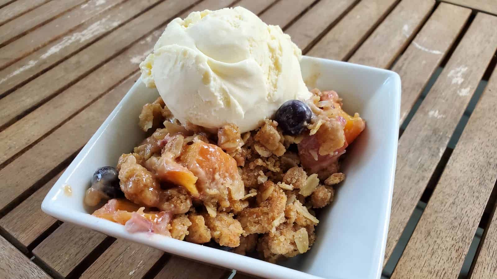 Blueberry peach crisp in a bowl with ice cream.